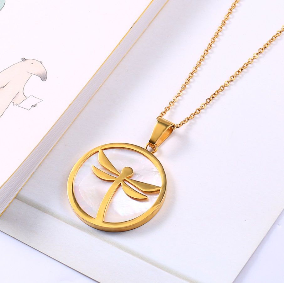 Detailed view of the gold dragonfly pendant on a shell background.